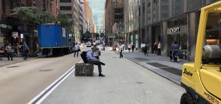 An image of E 43rd Shared St looking towards 3rd Ave. A man can be seen sitting on a granite block lining the new pedestrian space.