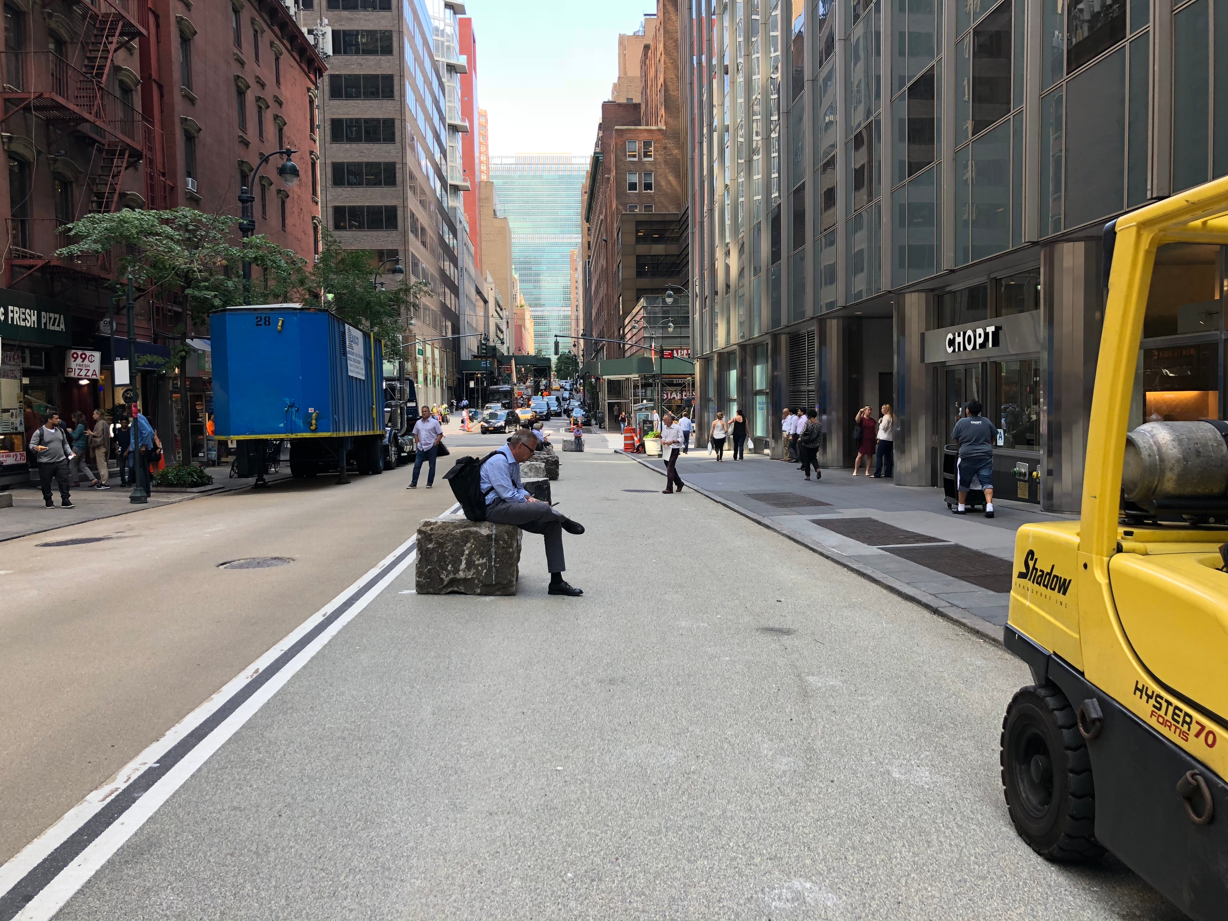 An image of E 43rd Shared St looking towards 3rd Ave. A man can be seen sitting on a granite block lining the new pedestrian space.