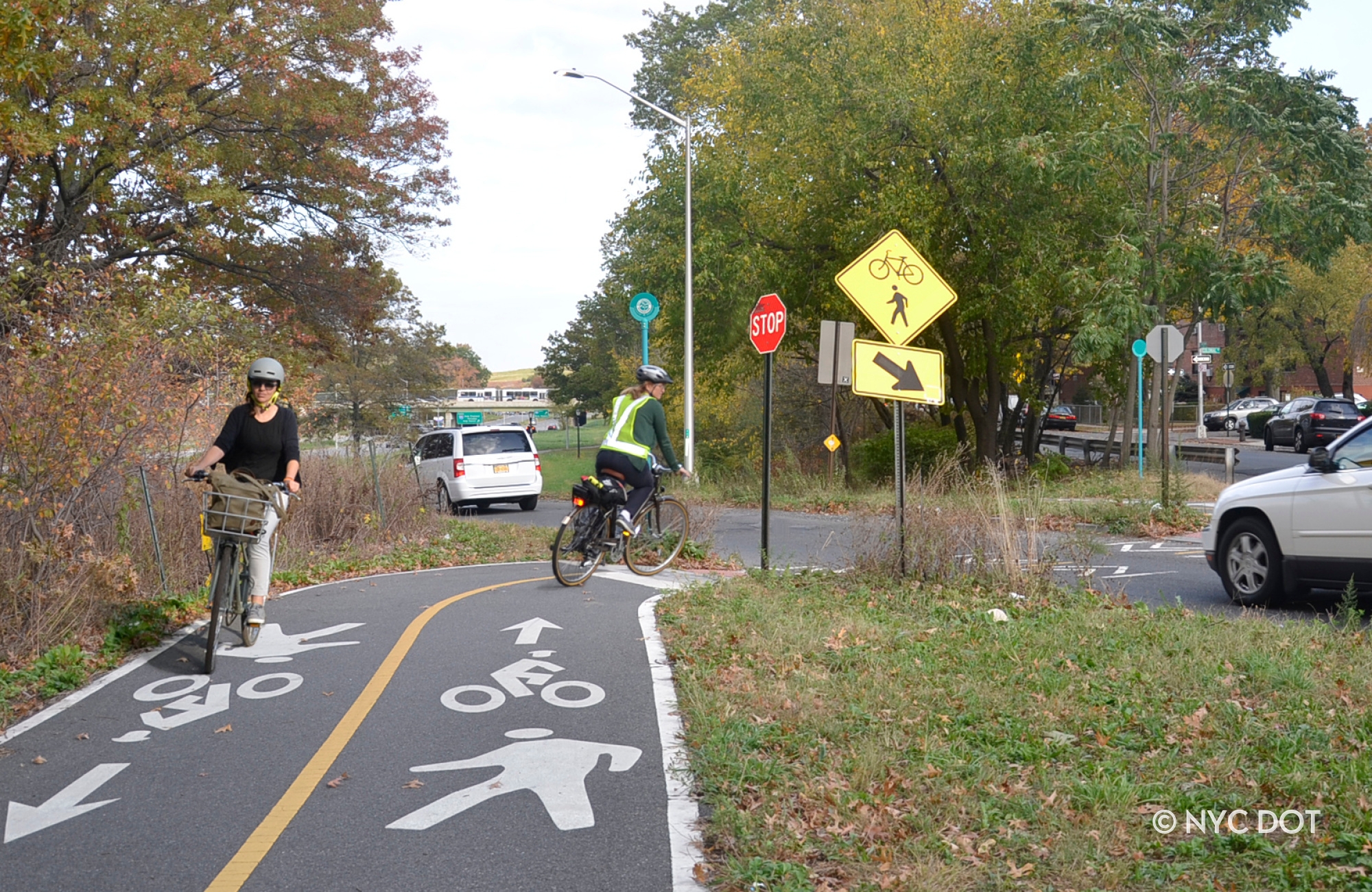 Two cyclists ride on painted separated bike lanes by Pelham Parkway in the Bronx.