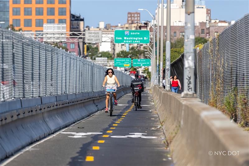 Two cyclists ride on new Washington Bridge protected bike lane.