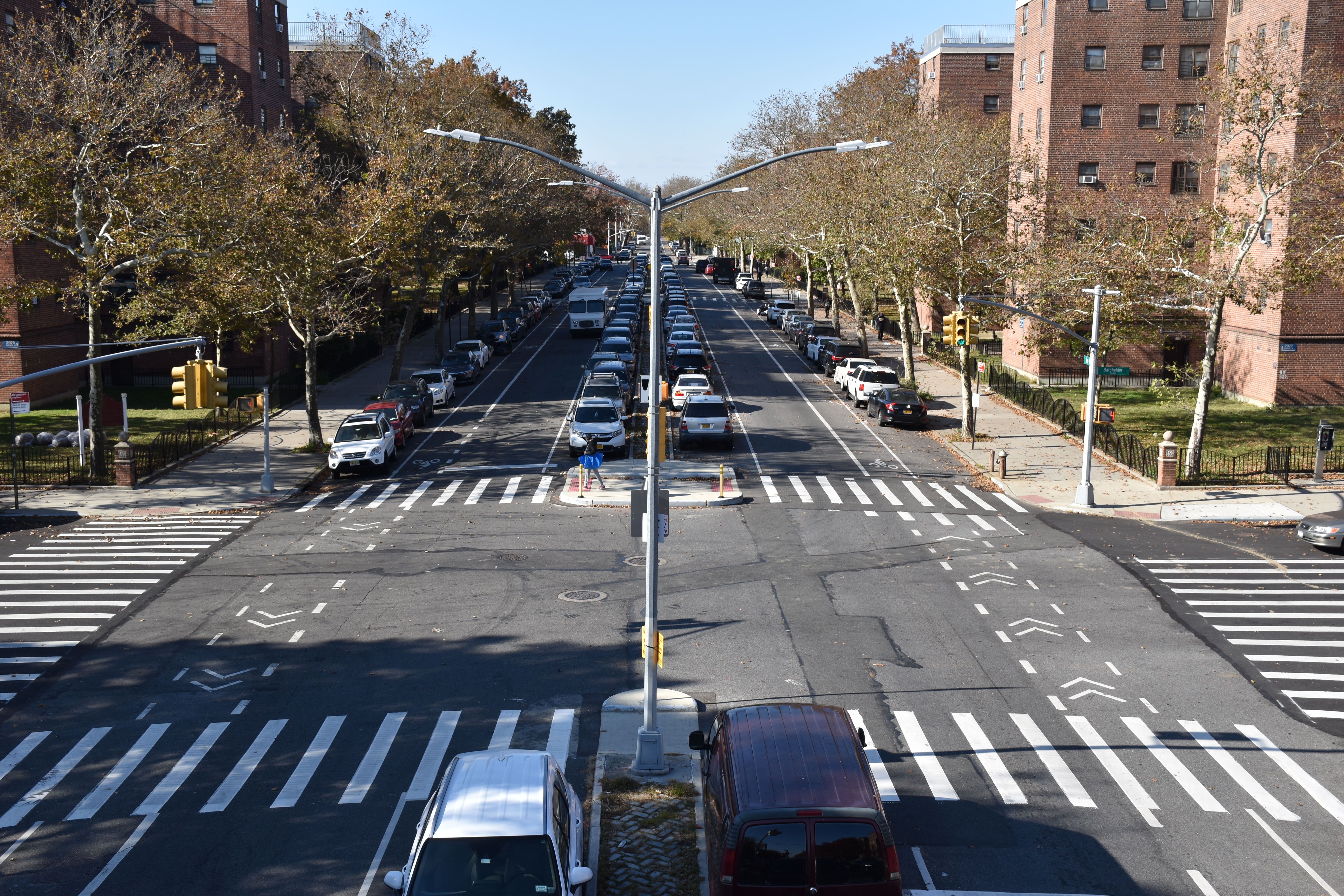 Birds eye view of an intersection with a two way street featuring four lanes of parking, pedestrian islands, and two-way bike lanes.