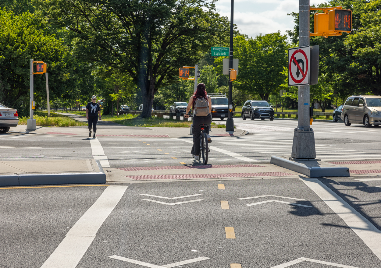 Cyclist and pedestrian cross newly-reconstructed intersection along Pelham Parkway.