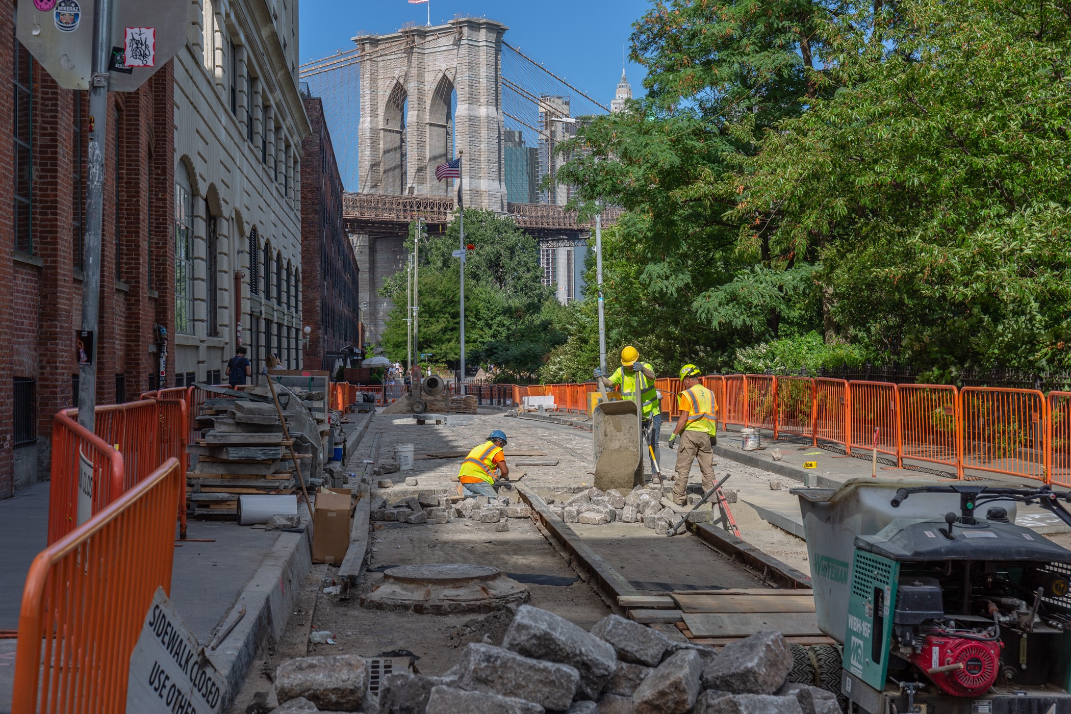 Workers on an roadway construction site in DUMBO with the Brooklyn Bridge in the background.