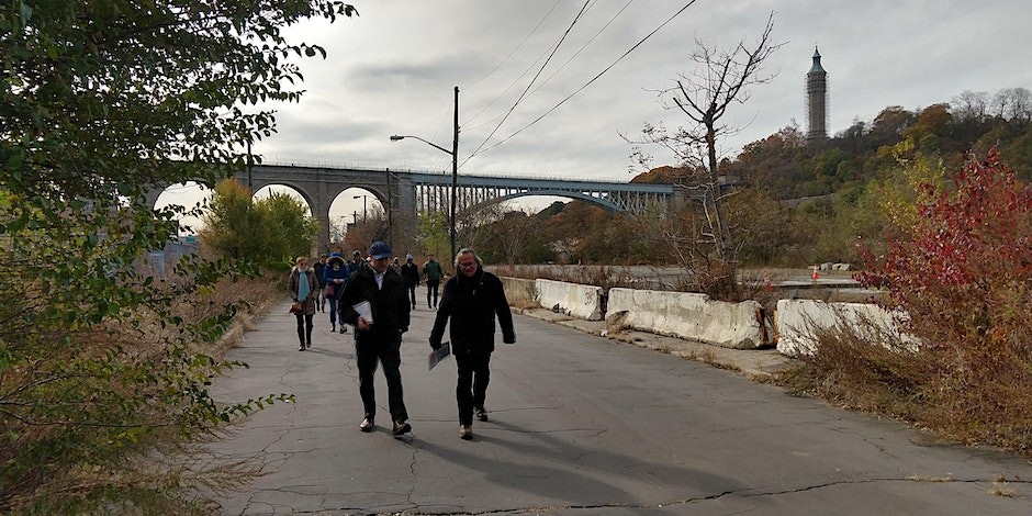 A group of people walk along the Harlem River on a cloudy day.