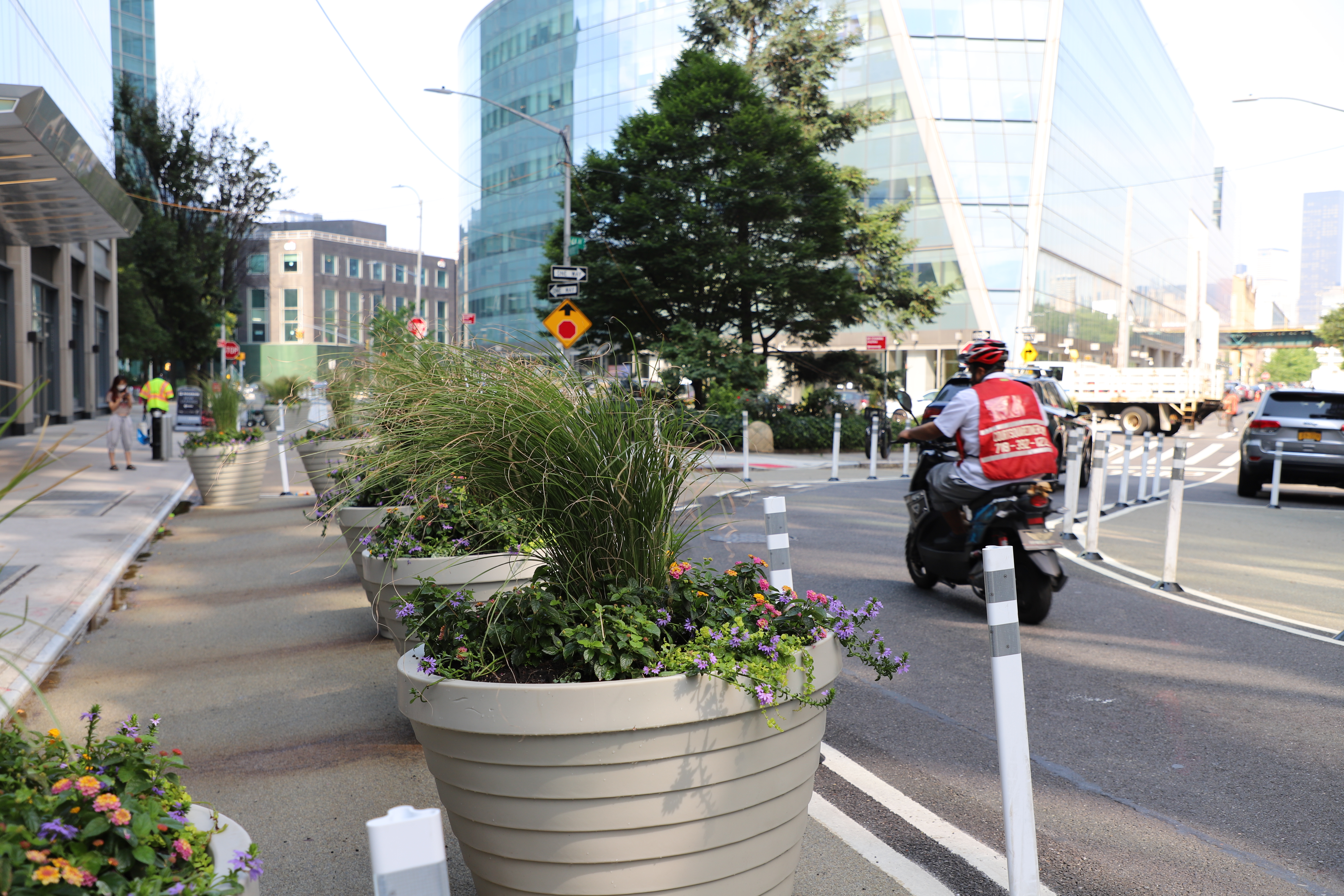 A motorcyclist using the Hunter Shared Street in Long Island City. In the foreground there is expanded pedestrian space lined with planters.