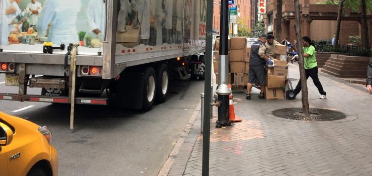 Image of a truck parked curbside along with driver and helpers in the act of delivering goods via hand trucks