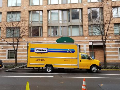 Yellow box truck unloading goods on Neighborhood Loading Zone in front of a large apartment building.