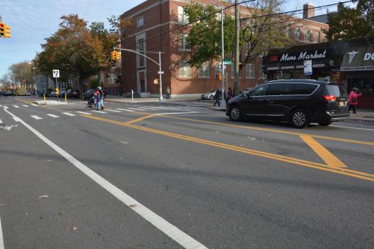 Pedestrians crossing on the crosswalk on Avenue X after improvements were implemented including pedestrian crosswalks, a pedestrian island, and channelization reducing the amount of active traffic lane.