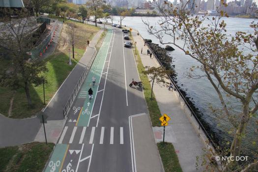 Aerial image of Shore Boulevard in Astoria Park in Queens. Three cyclists ride along the greenway abutting the East River.