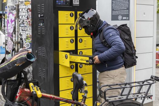 E-bike delivery worker wearing a helmet swaps an e-bike battery in a yellow compartment of a battery charging cabinet during the 2024 Public E-Bike Charging Pilot run by NYC DOT..
