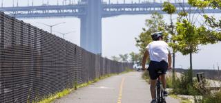 A cyclist rides along the Shore Parkway Greenway under the Verrazzano-Narrows Bridge