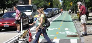 Pedestrians cross green cyclist path at crosswalk on Prospect Park West