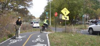 A cyclist rides in a separated bike path along Pelham Parkway.