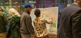 A city planner points at a map next to a member of the public at a public workshop.