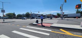 A pedestrian crossing Linden Blvd at Atkins Ave, pausing in a  newly constructed median tip 