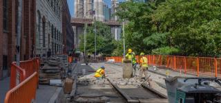 Workers on an roadway construction site in DUMBO with the Brooklyn Bridge in the background.